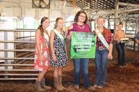 a group of girls standing in a barn holding a sign